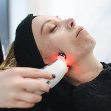 An adult woman receives a laser facial treatment in a modern skincare clinic.