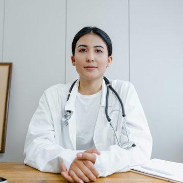 Young female doctor sitting at desk with stethoscope, ready for telehealth consultation.
